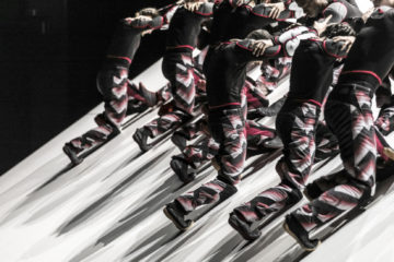 Skid Photo : Mat Backer sur une plateau ed scén inclinée, plsuieurs danseurs entremêlés forment comme un motif régulier