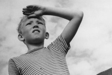 Trésors du doc - La Grande Aventure d'Arne Sucksdorff en noir et blanc, extrait de La Grande Aventure d'Arne Sucksdorff : un jeune garçon en contre plongée rregarde au loin, la main pour se protéger du soleil, sur son front