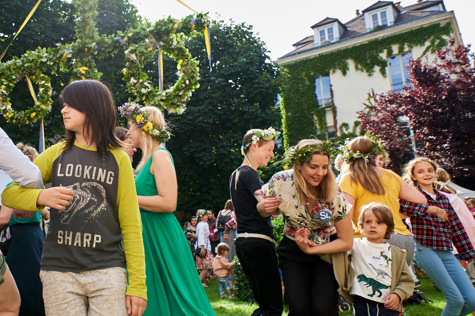 Photo de gens portant des couronnes de fleurs et dansant autour du mât fleuri dans le jardin de l'Institut suédois.