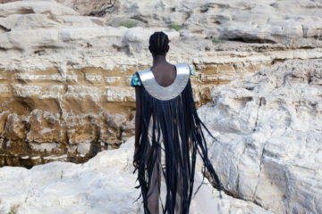 un mannequin de dos face à un paysage rocheux, porte une sorte de cape à franges un peu futuriste