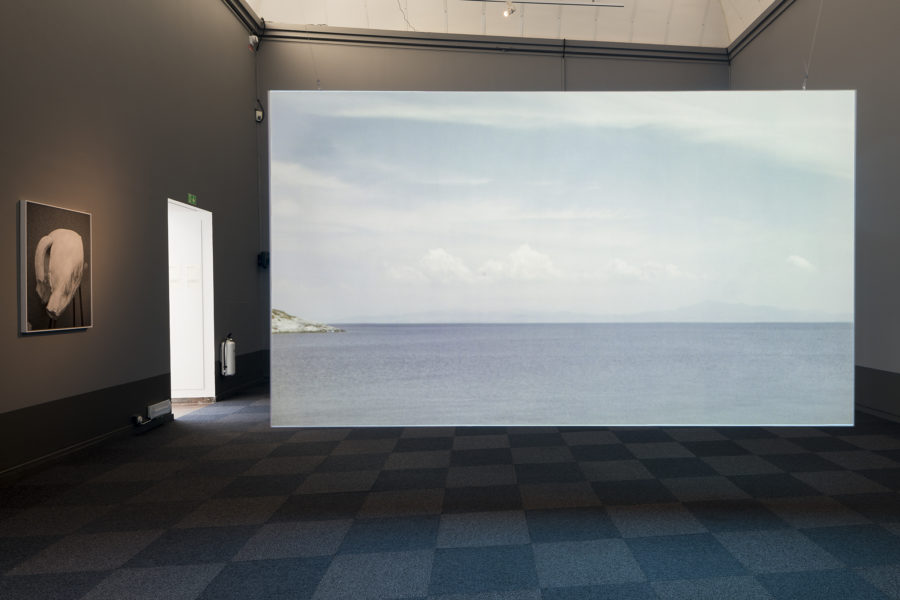 une pièce un peu sombre, une porte ouverte sur de la lumiére éclaire une grande toile au milieu de la pièce, représentant la mer et un horizon nuageux
