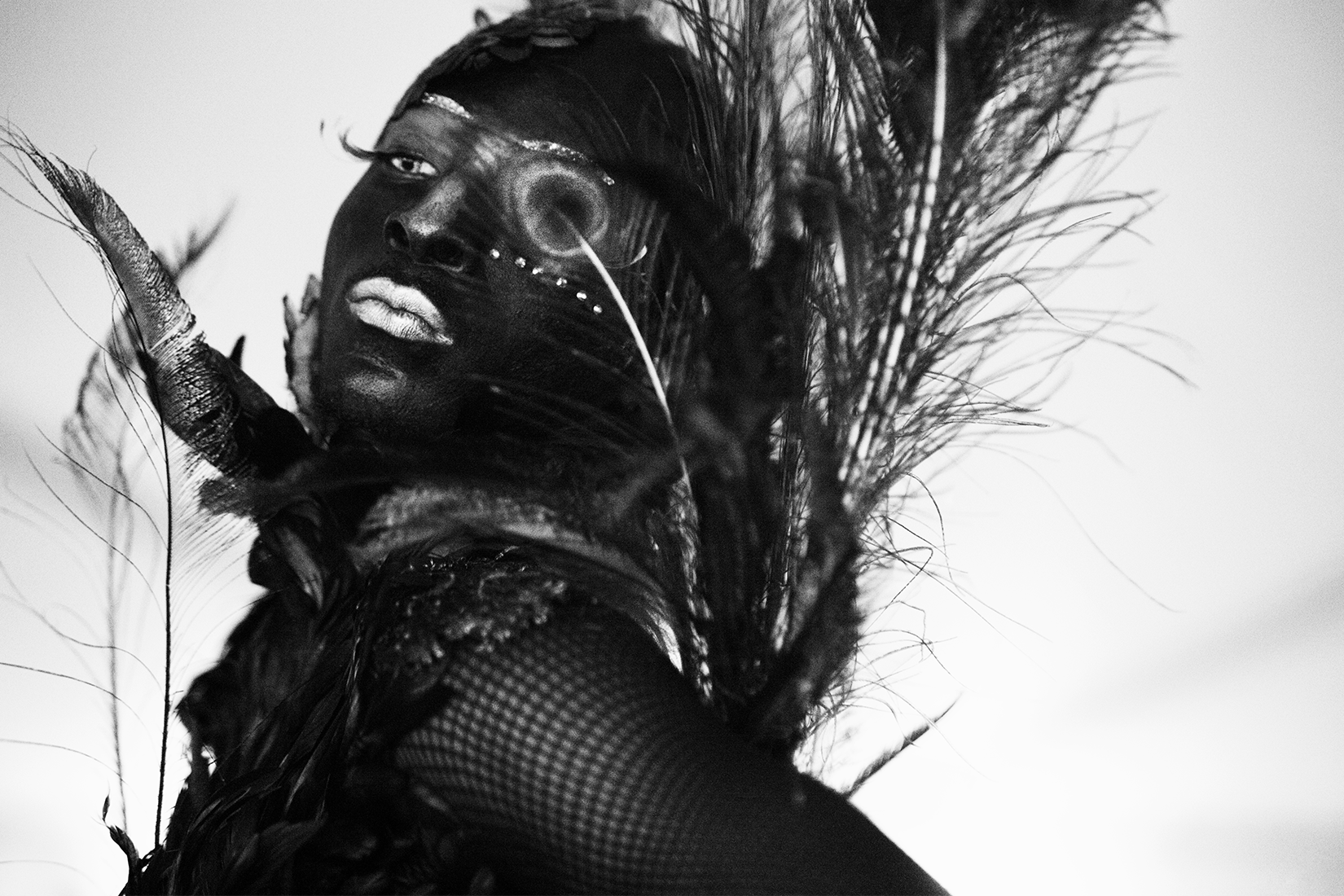 Black and white photo portrait of an artist dressed in feathers in voguing style.