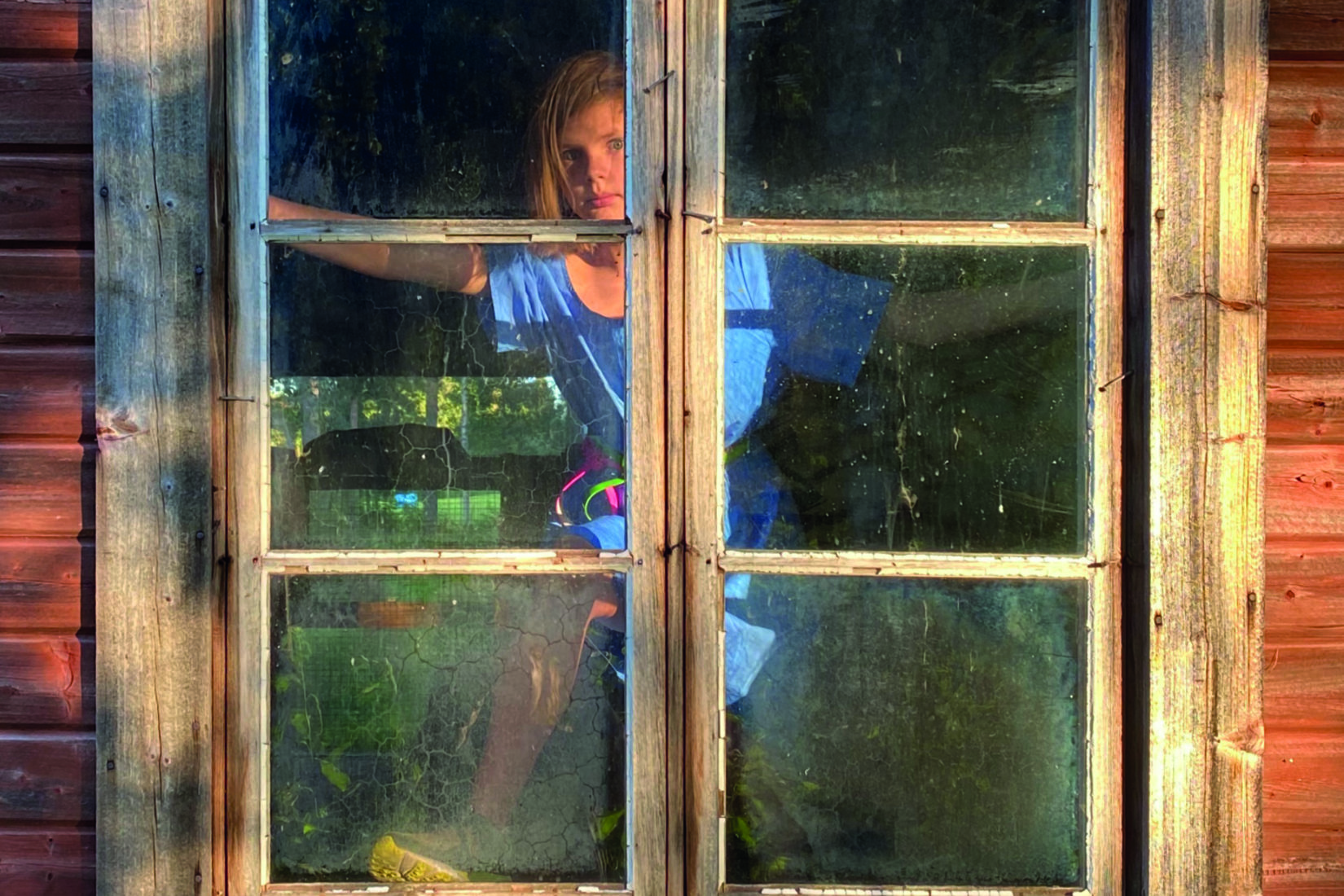 Une femme blonde debout derrière une vitre avec un pied sur le bord de la fenêtre
