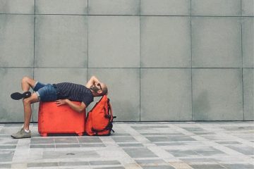 A man lying on a red travel bag