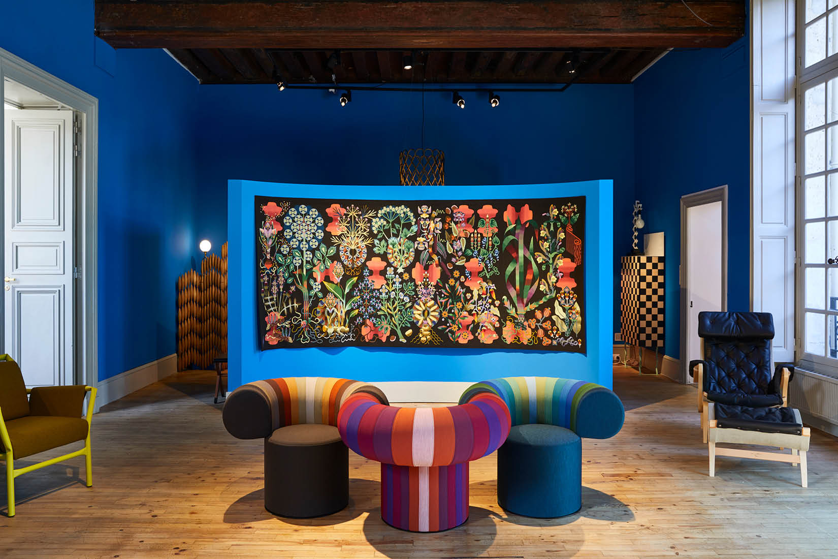 Exposition de la tapisserie Ras El Hanout de Pierre Marie avec en premier plan, trois fauteuils colorés de Blå Station.