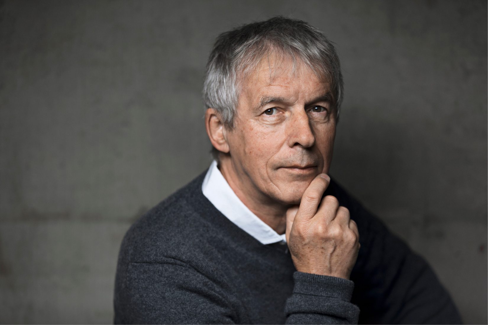 Photo de Jean-Claude Mourlevat sur fonds gris, se tenant le menton.