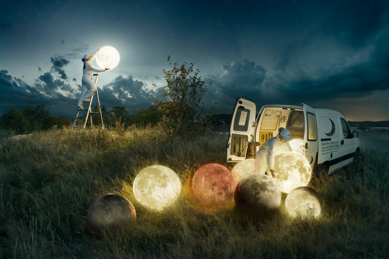 Photo représentant un employé en uniforme blanc accrochant une nouvelle pleine lune dans le ciel pendant son collègue range un stock de pleines lunes dans le coffre d'une camionnette de service.