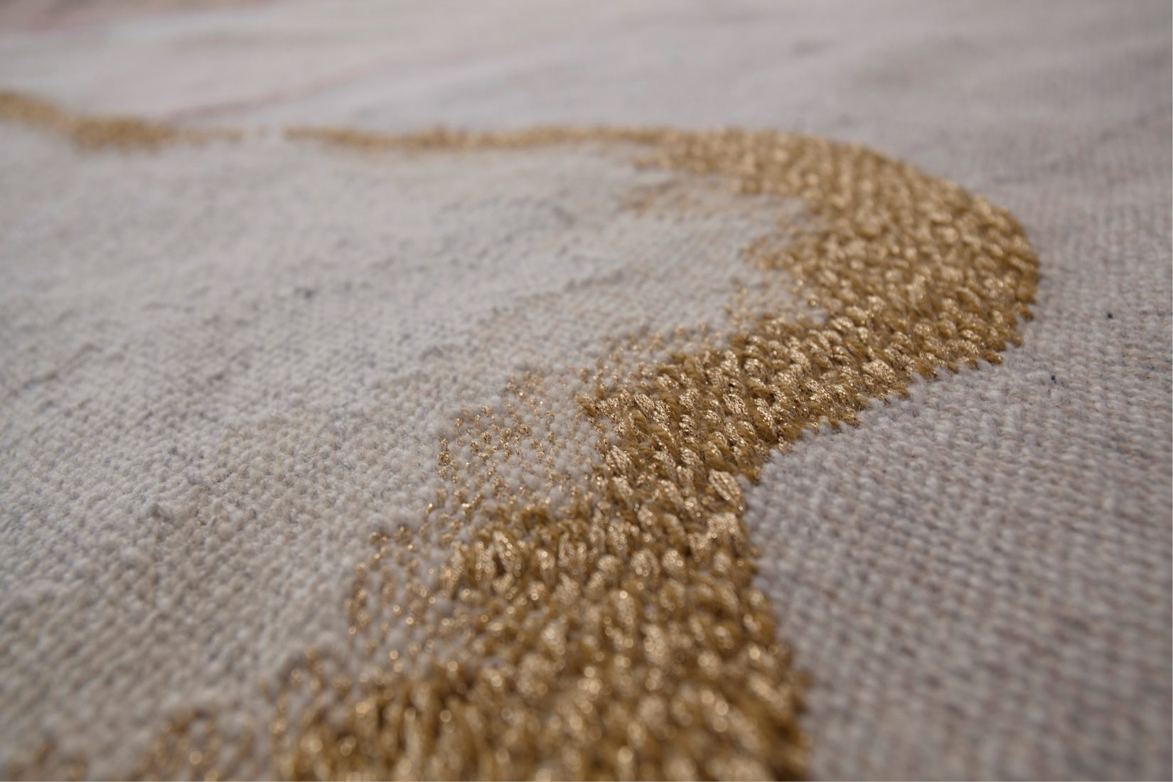 Detail of a weaving showing a golden curve on a light-coloured background.