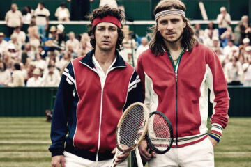 Les acteurs jouant Björn Borg et John McEnroe posant côte-à-côte sur un court de tennis, avec des spectateurs derrière eux.