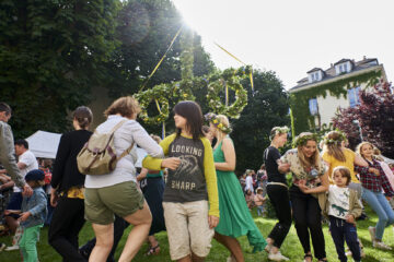 Photo prise dans le jardin de l'Institut suédois, avec des visiteurs dansant autour d'un mât fleuri.