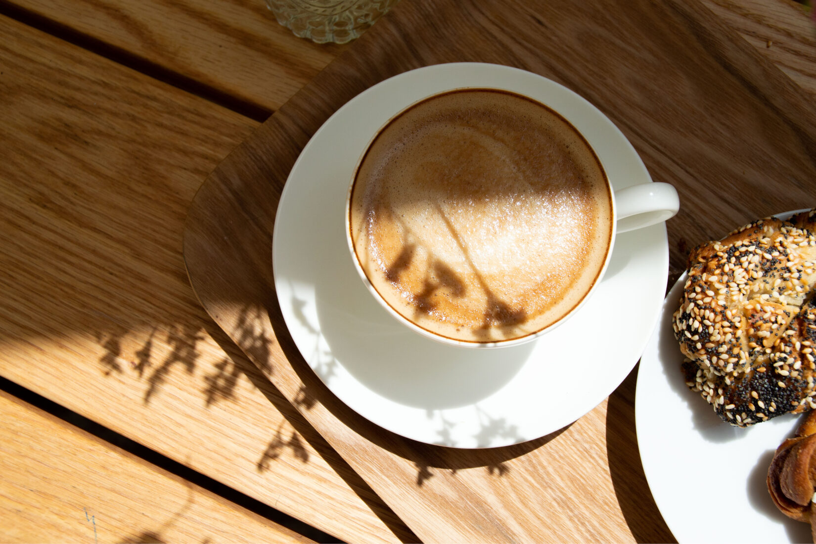 Café au lait et assiette de gâteaux posés sur une table en bois baignée d'ombre et de lumière.