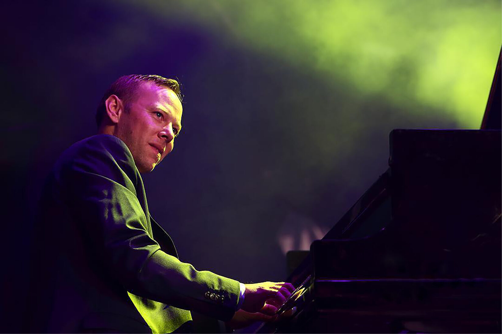 Photo of Mattias Nilsson at the piano, with a ray of yellow-green light over him.