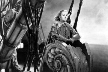 Black and white photography of Greta Garbo as Queen Christina, standing on a boat with her eyes towards the horizon.