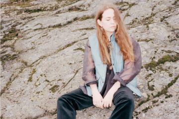 Alice Boman assise sur des rochers, les yeux fermés, cheveux dans le vent.
