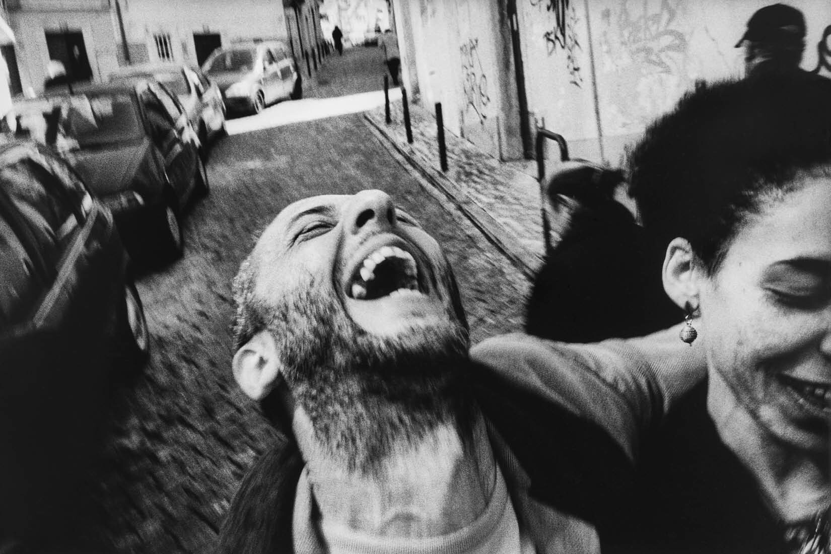 Photo en noir et blanc d'un homme rit dans une rue pavée.