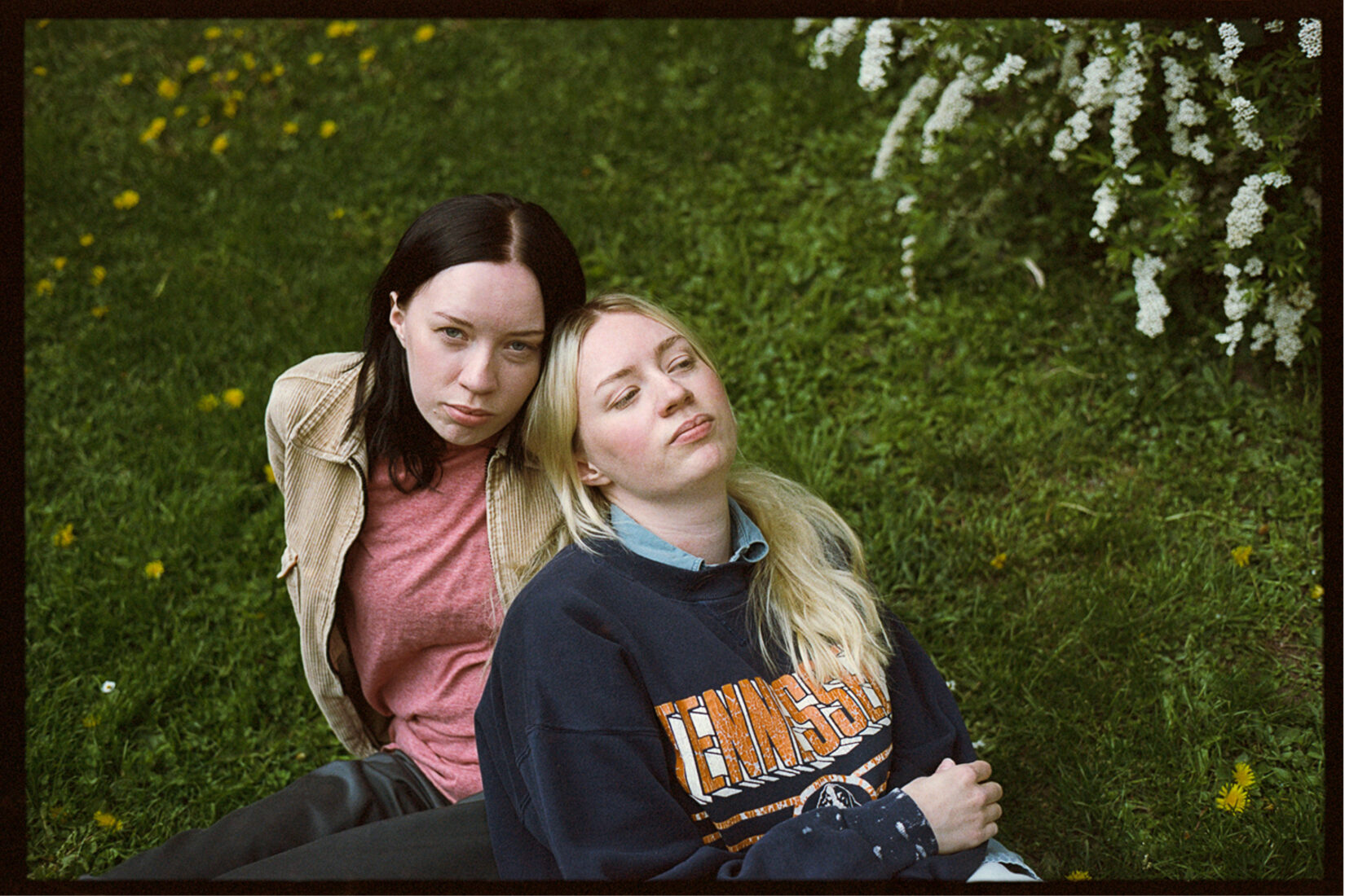 Two young women are sitting in the grass close to each other.