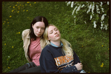 Deux jeunes femmes sont assises dans l'herbe, l'une contre l'autre.