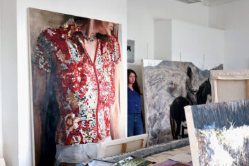 L'artiste Sara-Vide Ericson dans son atelier, debout entre ses grandes toiles.