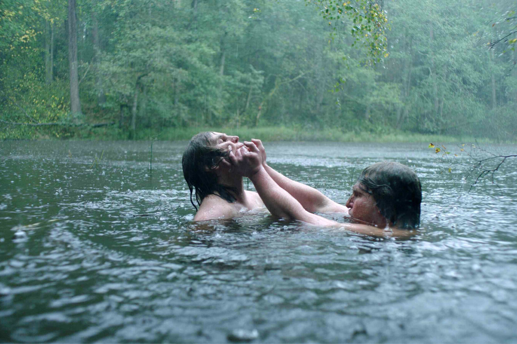 Two people are immerged in a lake or a river, in the rain, fighting with one another.