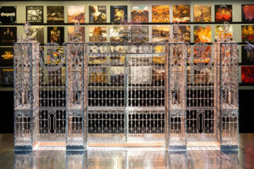 photo d'une porte métallique en argent dans un espace d'exposition sombre avec plein d'affiche derrière