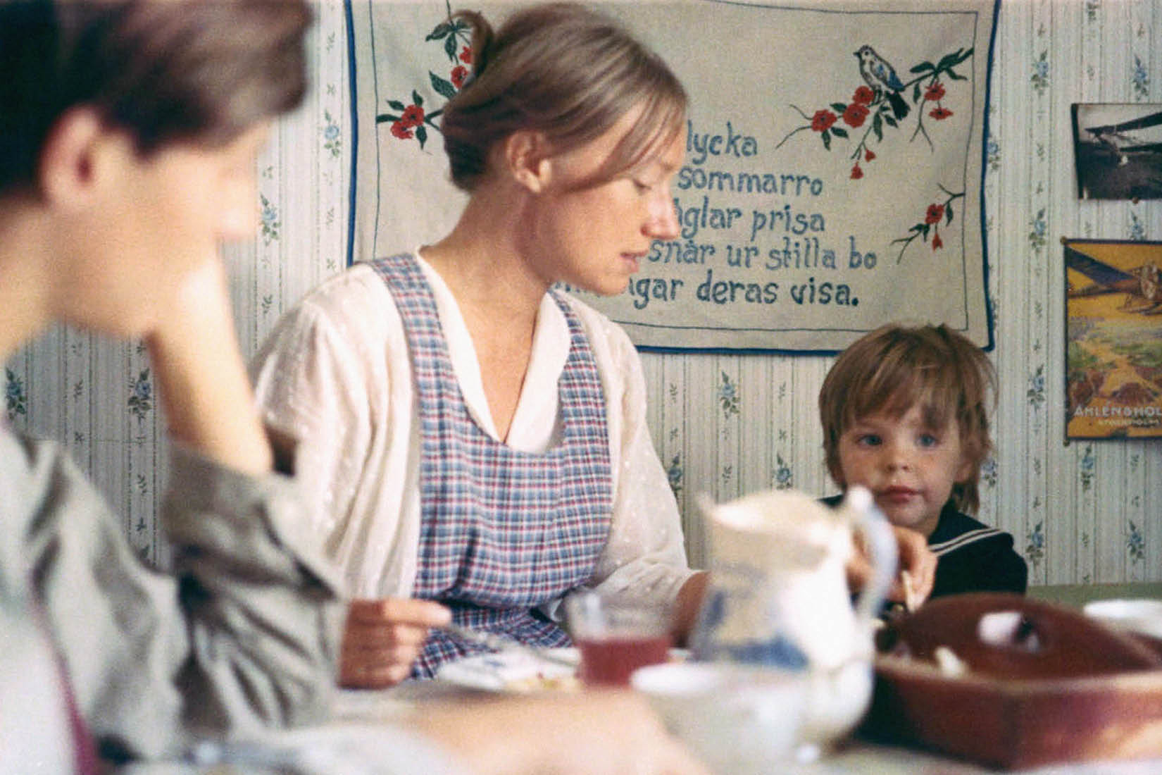 Trois personnes sont attablées dans une cuisine, dont une jeune femme qui aide son petit garçon à manger.