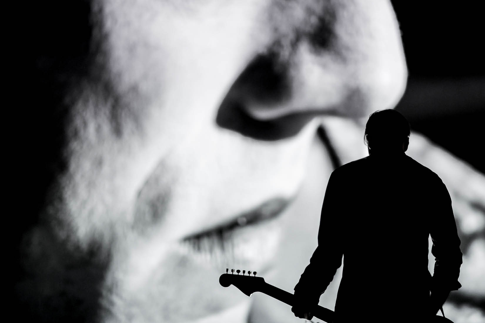 Visage en noir et blanc sur un écran en fond et ombre de musicien devant