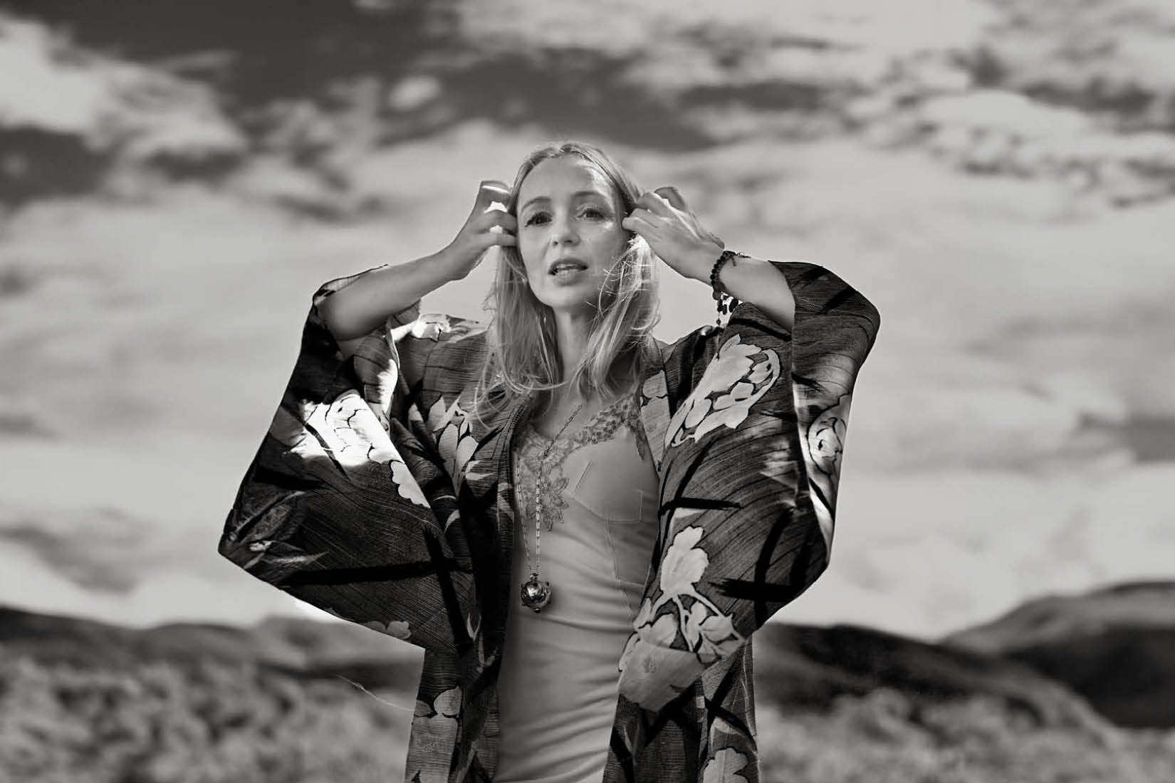 Photo en noir et blanc de Lisa Ekdahl portant un kimono à larges manches, sur fond de ciel tourmenté.