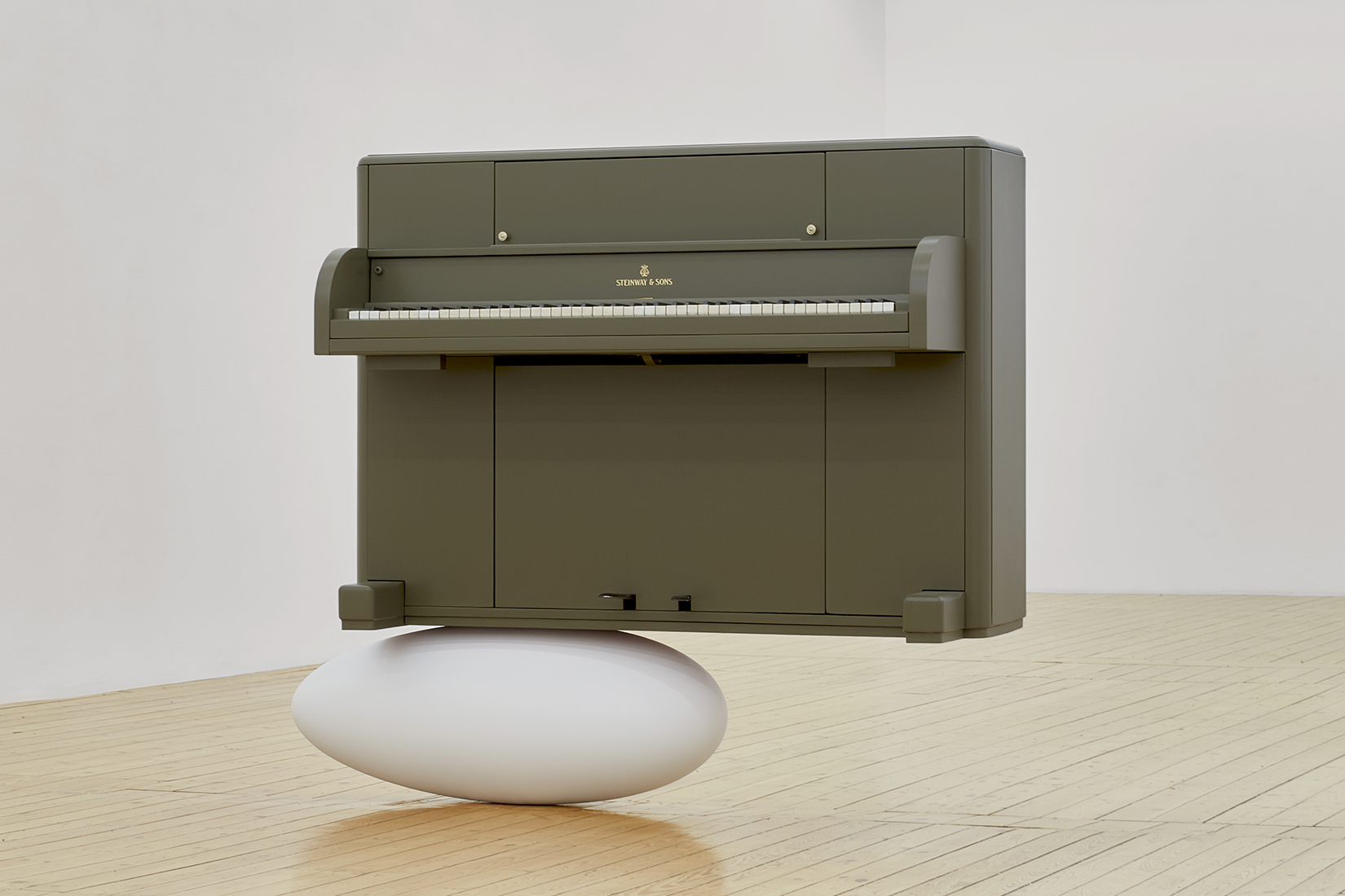 Photo d'un piano perché en équilibre sur ce qui ressemble à un oeuf oblong, au milieu d'une salle vide.