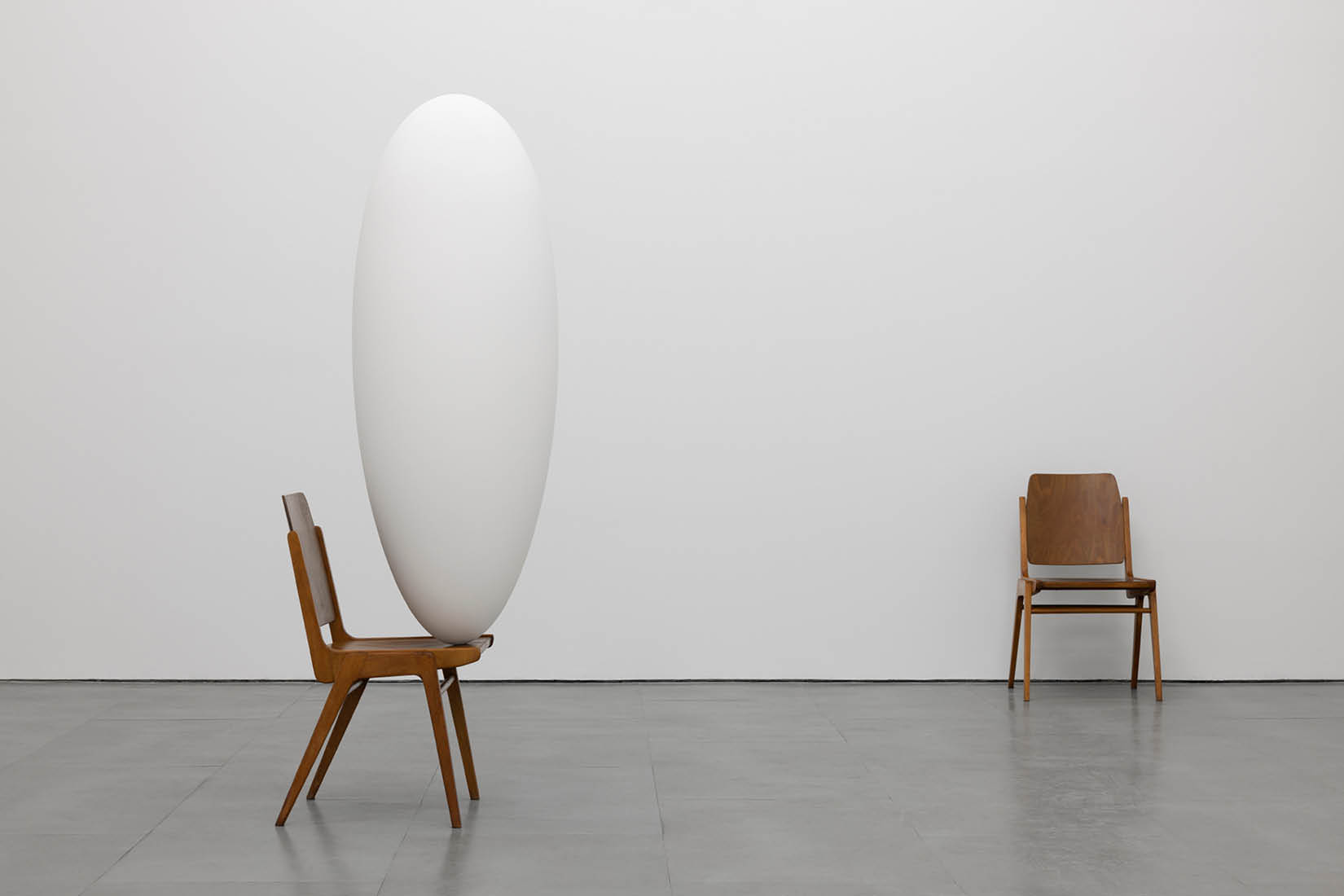 Photo of two chairs in a light and empty room: one of them is bearing a tall white cocoon on the verge of its seat.