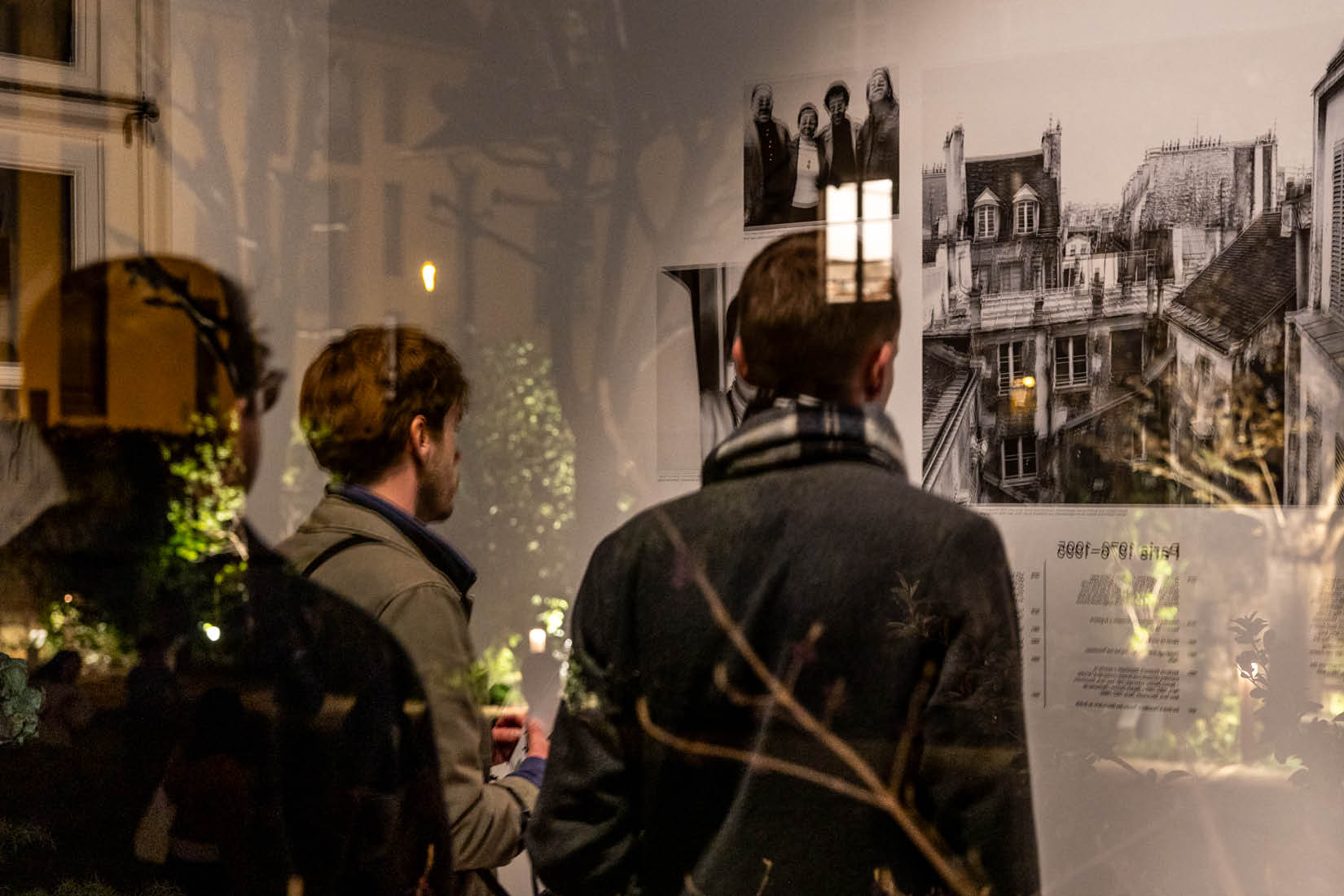 Visitors photographed from behind, through a window on which trees reflect tehmselves.