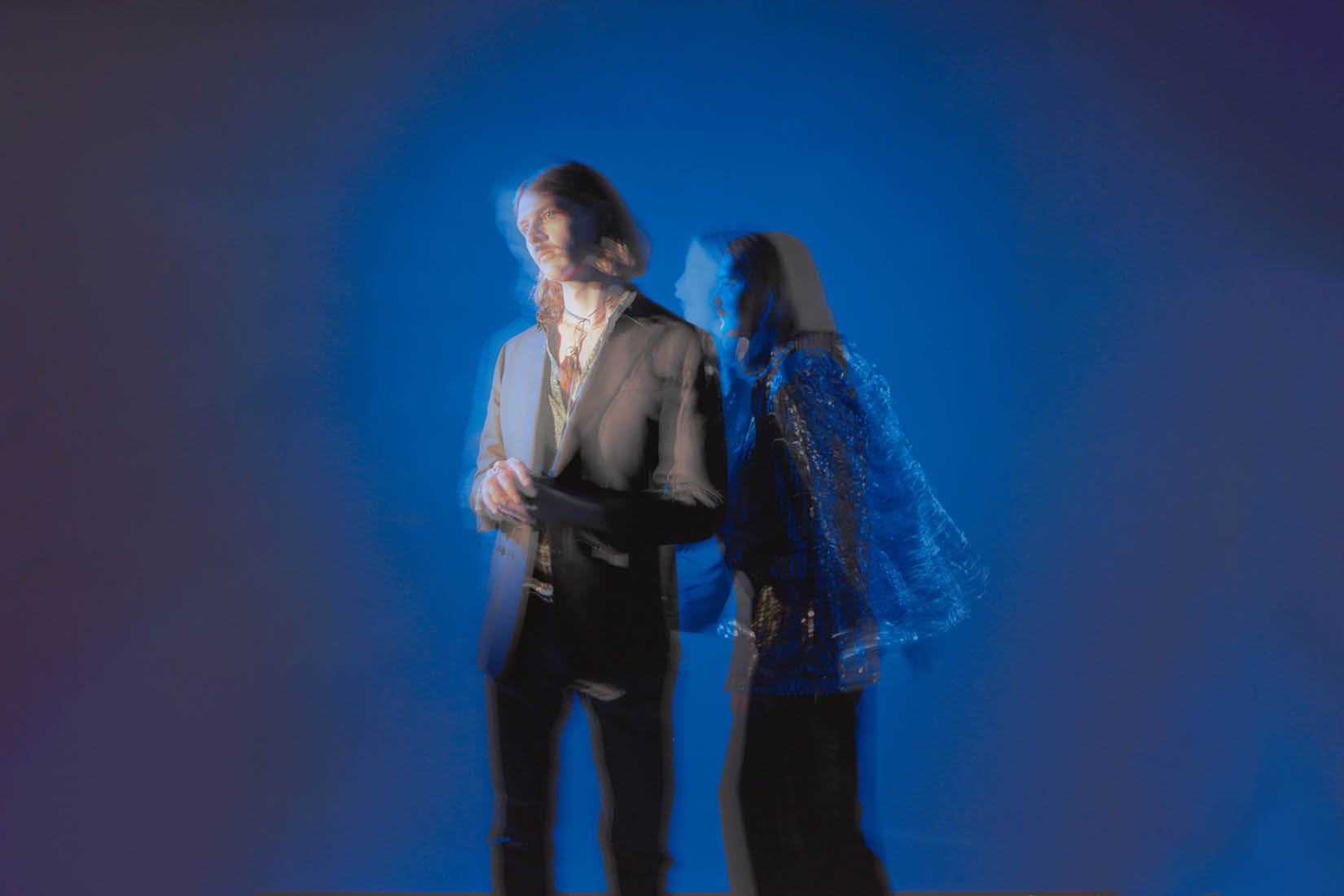 Image onirique et floue des deux chanteurs se tenant dans un espace bleu nuit.