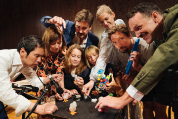 Photo of a group of people leaned over a table, playing with objects.