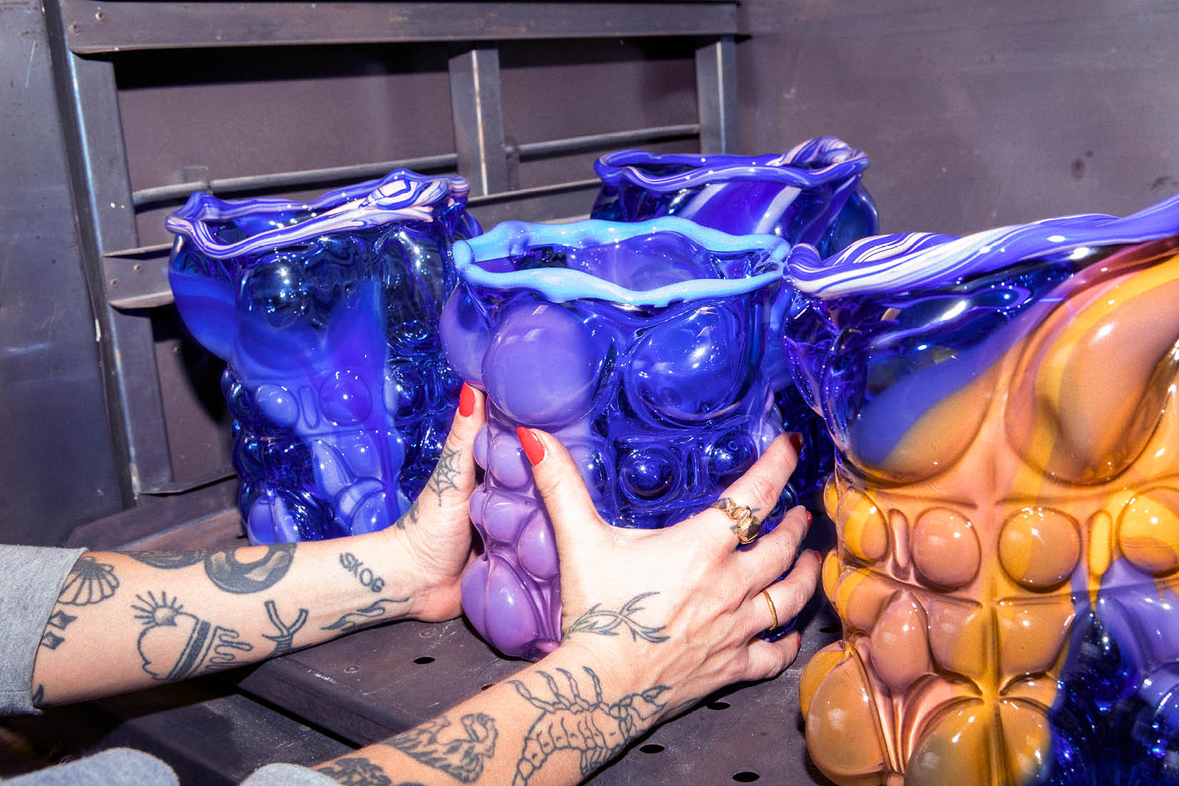 Mains de femme tatouées se saissant d'une sculpture en verre sur une étagère.