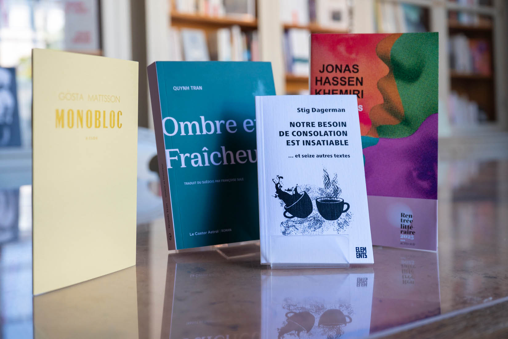 Quatre livres posés sur une table et bibliothèque à l'arrière-plan.