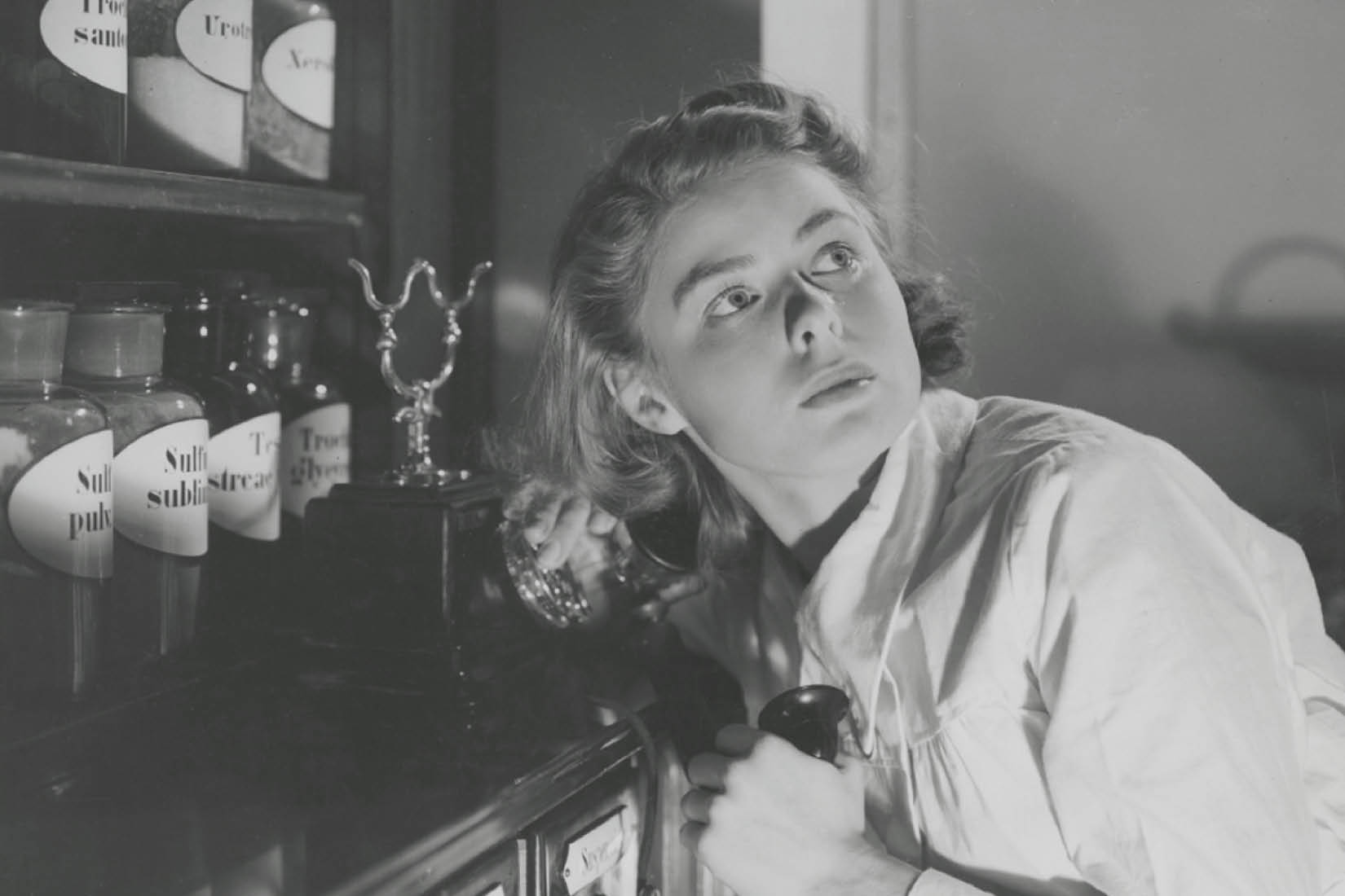 Photo en noir et blanc d'une jeune femme dans ce qui ressemble à une cuisine, se retournant l'air inquiet.