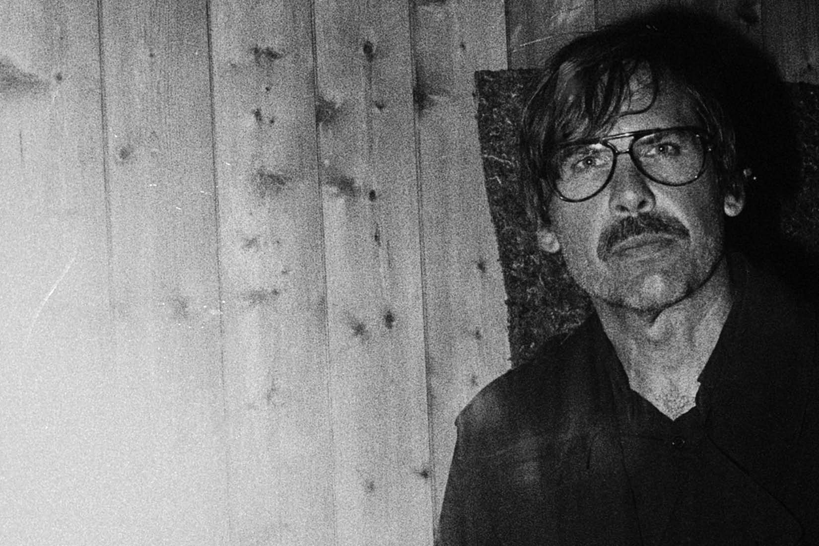 Photo en noir et blanc d'un homme à moustache et à lunettes.