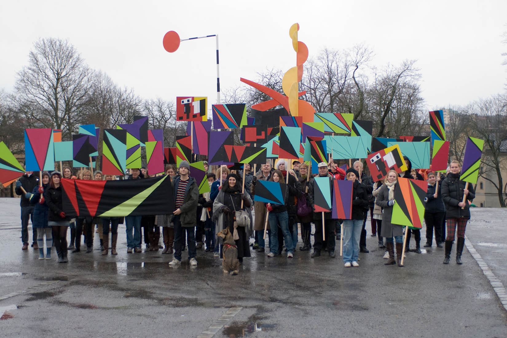 Groupe de gens dans la rue brandissant des pancartes avec des motifs géométriques colorés.